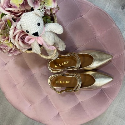 Sapatos dourados femininos sobre puff rosa com urso de crochê e flores artificiais