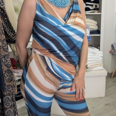 Mulher com macacão de riscas azul, branco e castanho e colar azul em loja de roupa