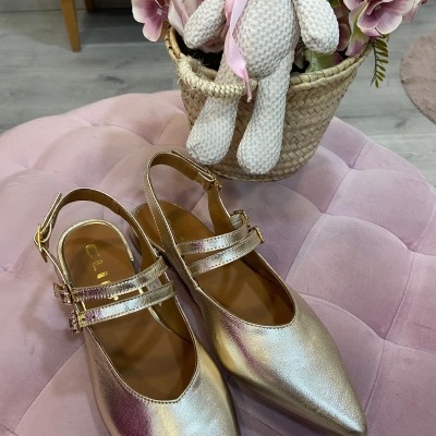 Sapatos metálicos prateados com bico fino e alças num pufe rosa com flores e ursinho