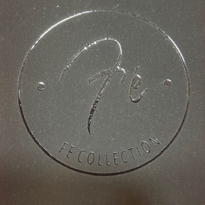 Logo redondo em relevo com texto 'fe' e 'FE COLLECTION'