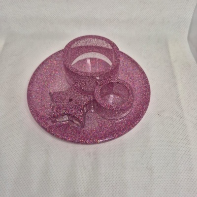 Suportes redondos e estrela em resina rosa com glitter sobre superfície branca.