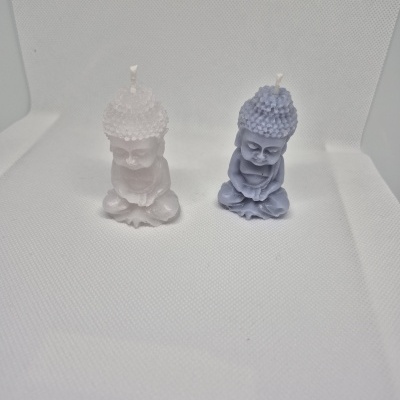 Duas velas em forma de Buda, branca e azul claro, em fundo branco texturado.