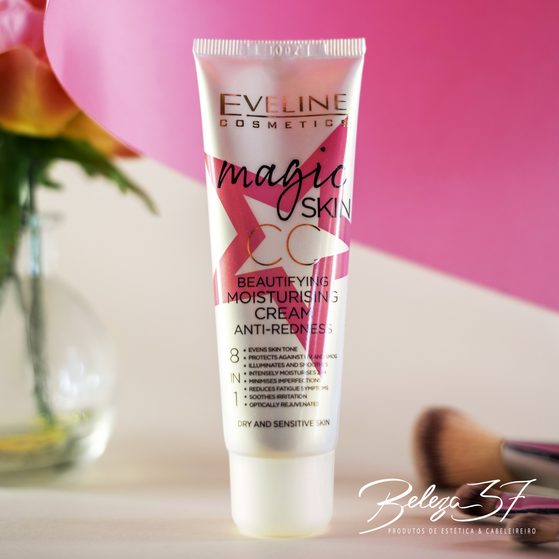 Creme Eveline Magic Skin CC Anti-Redness 50ml Tubo de creme hidratante Eveline Cosmetics Magic Skin CC num fundo rosa com pincel de maquilhagem ao lado