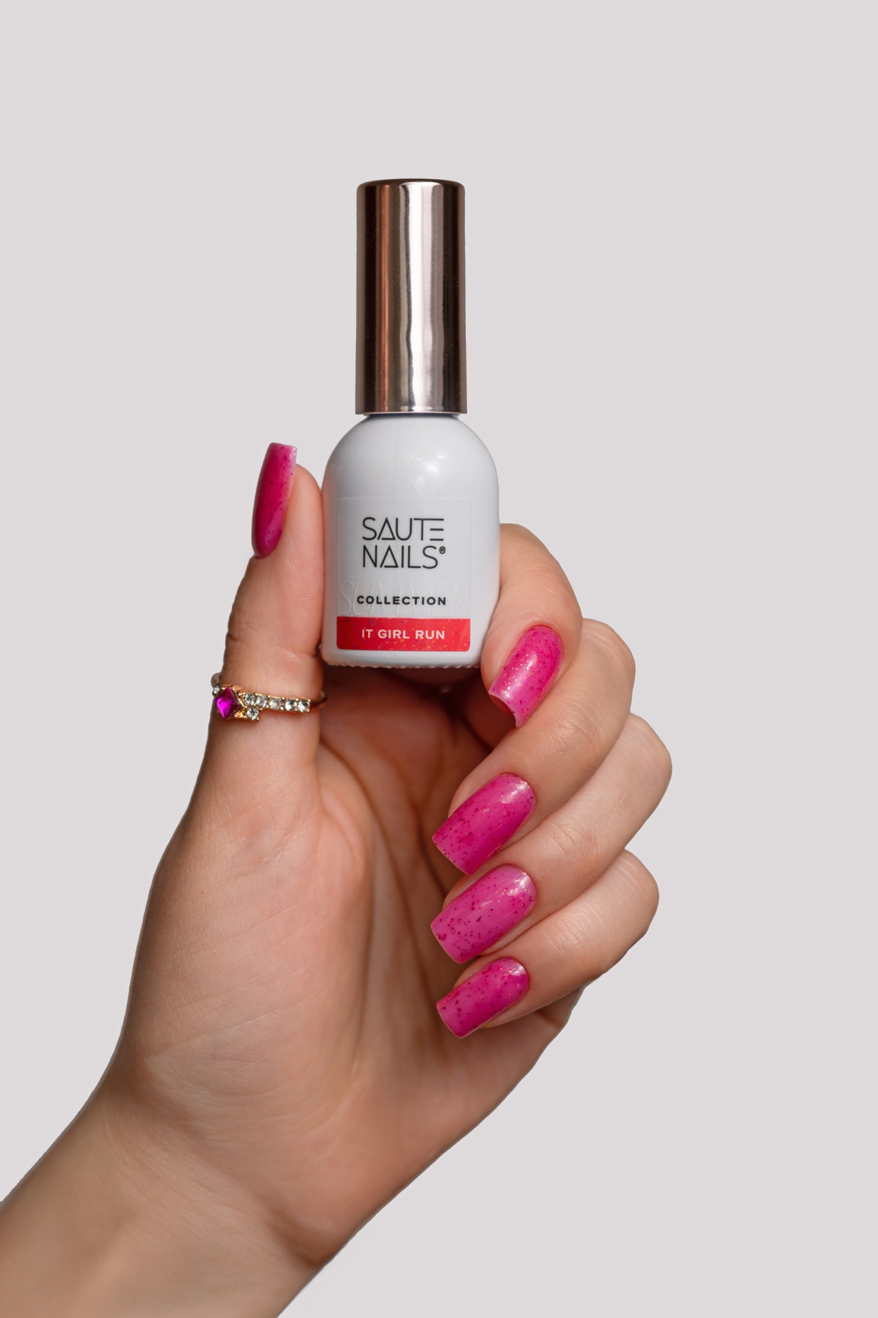 Verniz Gel It Girl Run (Rosa Néon com partículas Rosa Escuro) Frasco branco de verniz de unhas com tampa prateada segurado por mão com unhas cor rosa brilhantes