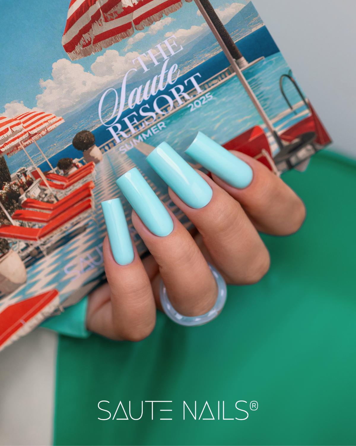 Coleção de Verniz Gel Saute Resort (6 Cores) Unhas azuis compridas segurando cartão de praia com texto THE Saute RESORT SUMMER 2025