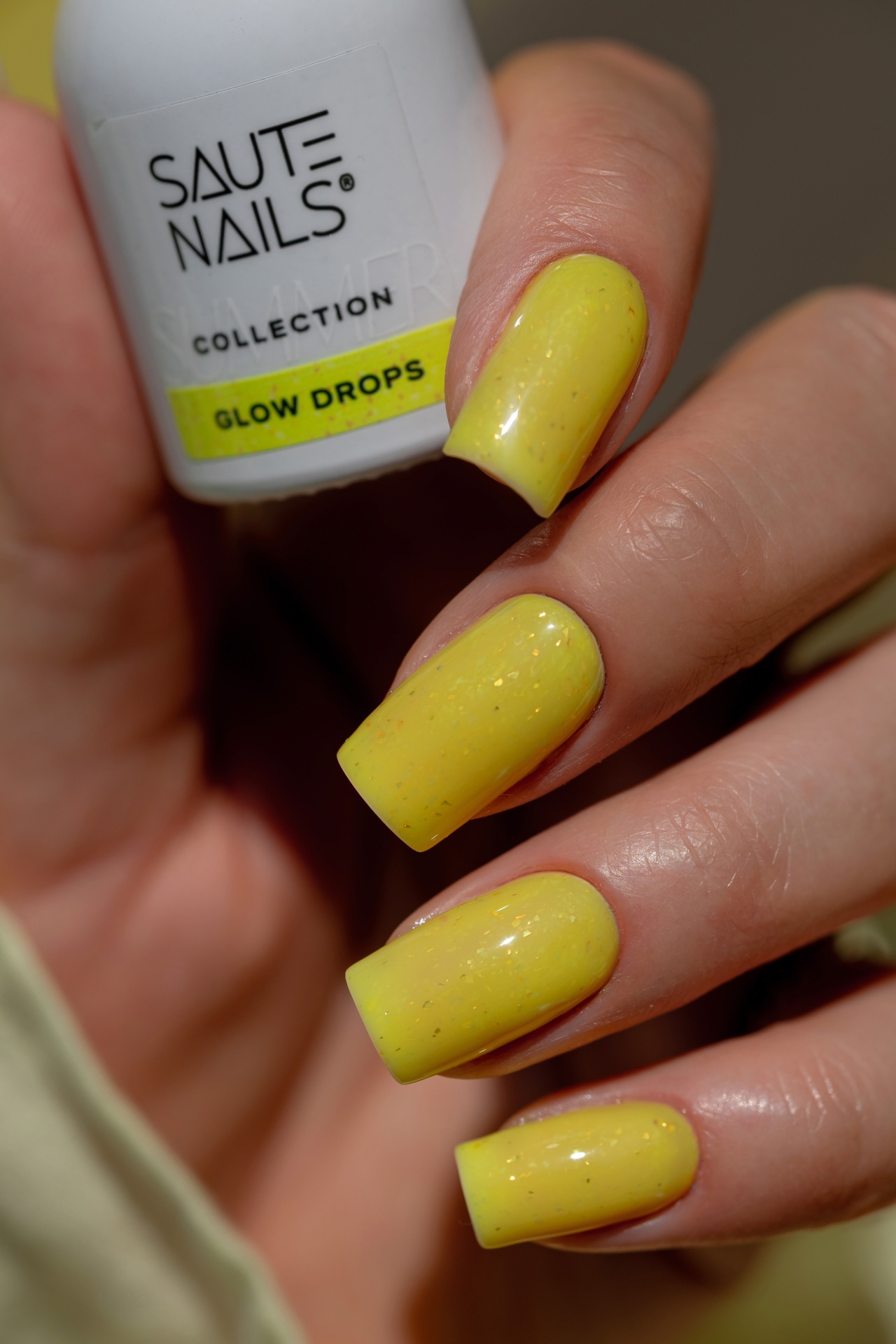 Verniz Gel Glow Drops (Amarelo Intenso com Partículas Douradas) Esmalte amarelo com brilho aplicado em unhas compridas quadradas da marca SAUTE NAILS.