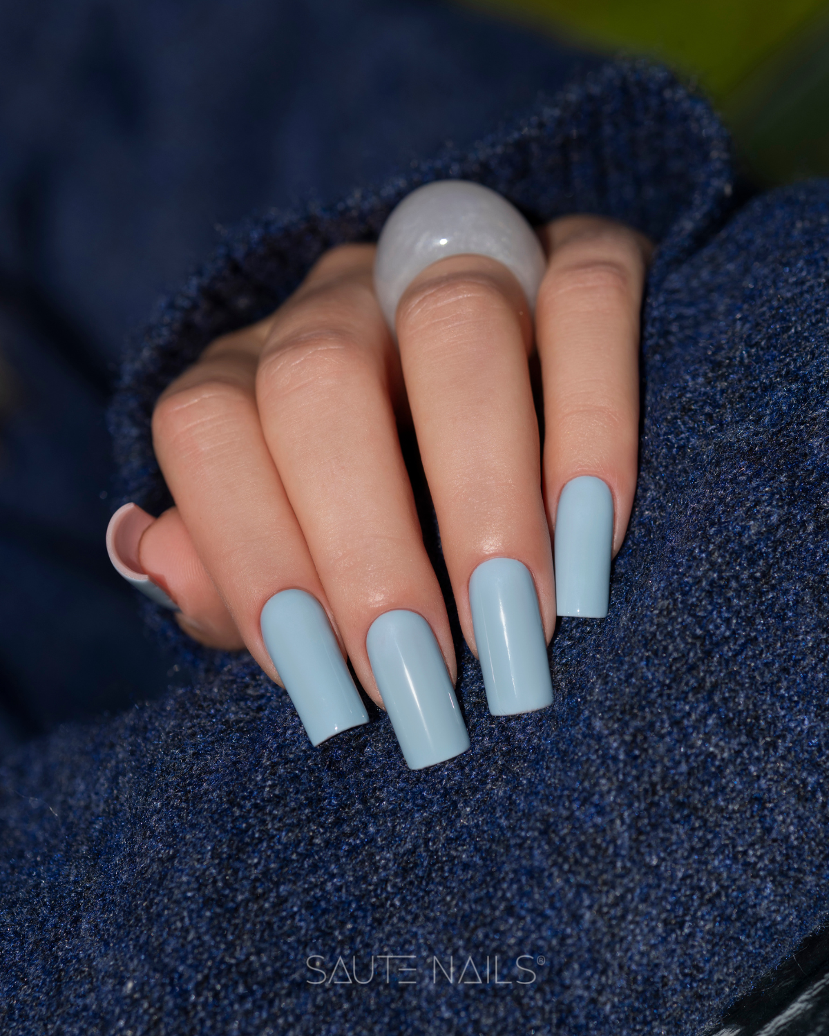 Verniz Gel Saute Nails S329 - Saute Blue (Azul Suave) Unhas compridas azuis claras brilhantes em mão feminina com anel transparente e roupa azul escura