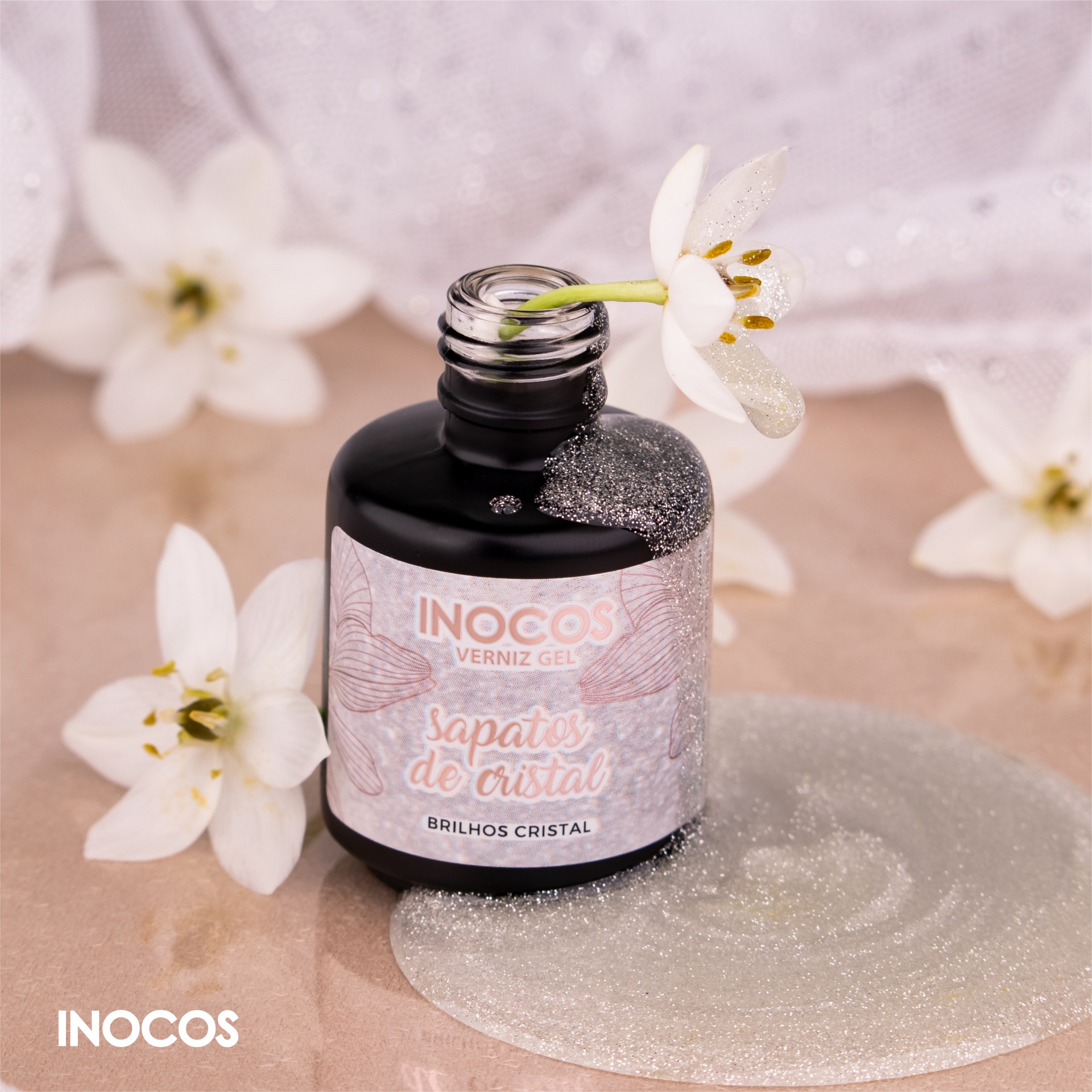 Verniz Gel Inocos – 321 - Sapatos de Cristal Frasco preto de verniz gel com rótulo branco e rosa da marca INOCOS e flores brancas ao redor