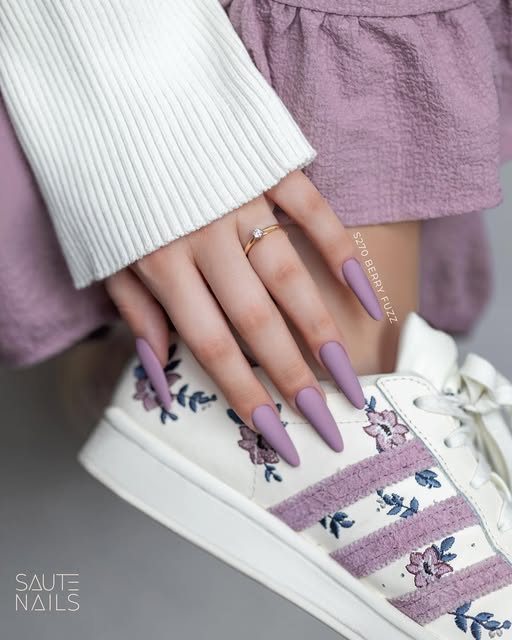 Verniz Gel Saute Nails S270 - Berry Fuzz (Roxo Amora) Mãos com unhas lilás fosco segurando ténis branco com riscas e bordados lilás