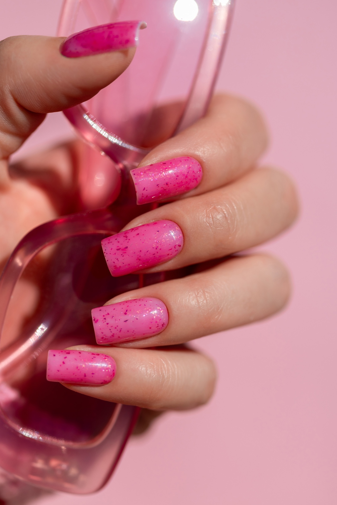 Verniz Gel It Girl Run (Rosa Néon com partículas Rosa Escuro) Mãos com unhas postiças rosa de glitter segurando objecto plástico transparente