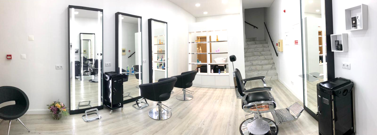 Interior de sala de cabeleireiro com cadeiras pretas, espelhos grandes e piso claro