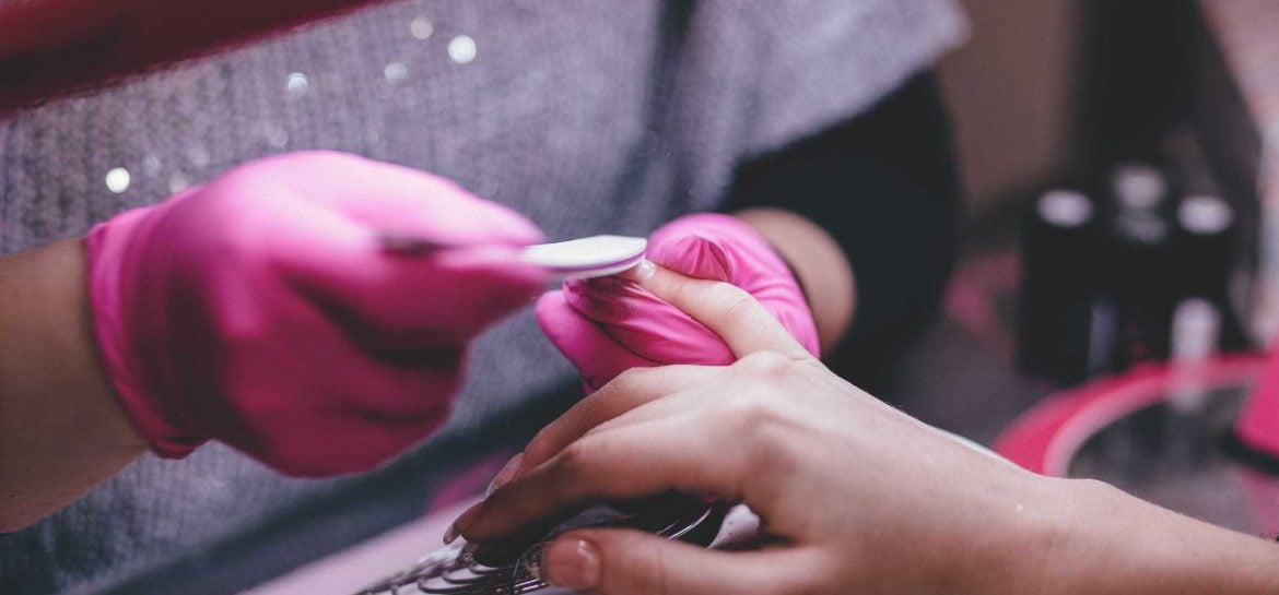 Procedimento de manicure com luvas cor-de-rosa e lixa branca nas unhas