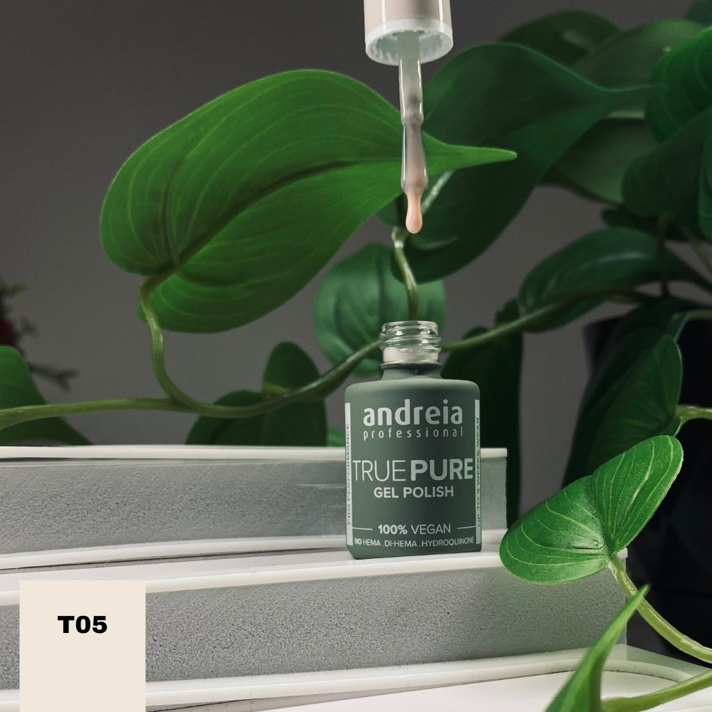 The Gel Polish Andreia True Pure T05 - Milky Nude (Nude Leitoso) Frasco de verniz gel nude Andreia True Pure T05 com conta-gotas sobre superfícies cinzentas e plantas verdes