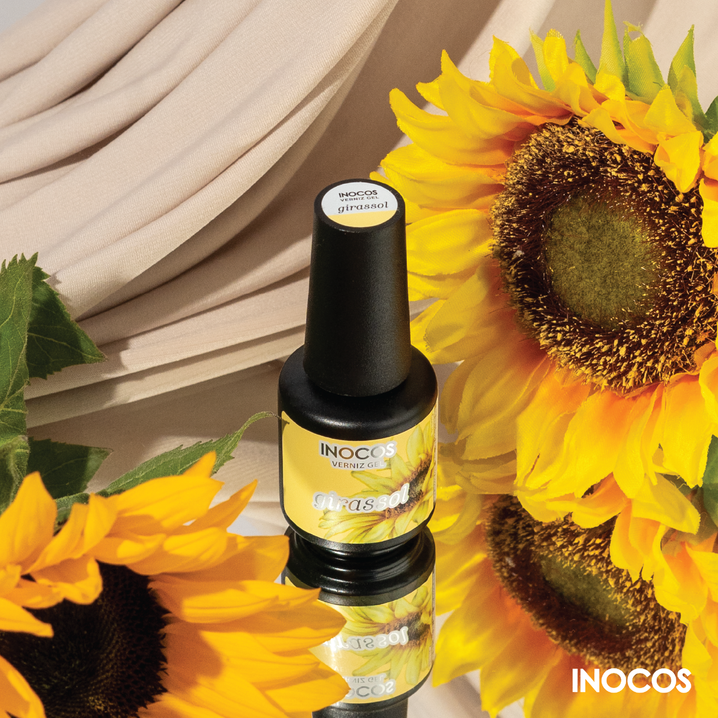 Verniz Gel Inocos – 379 - Girassol Frasco de verniz gel INOCOS rodeado por girassóis sobre superfície espelhada