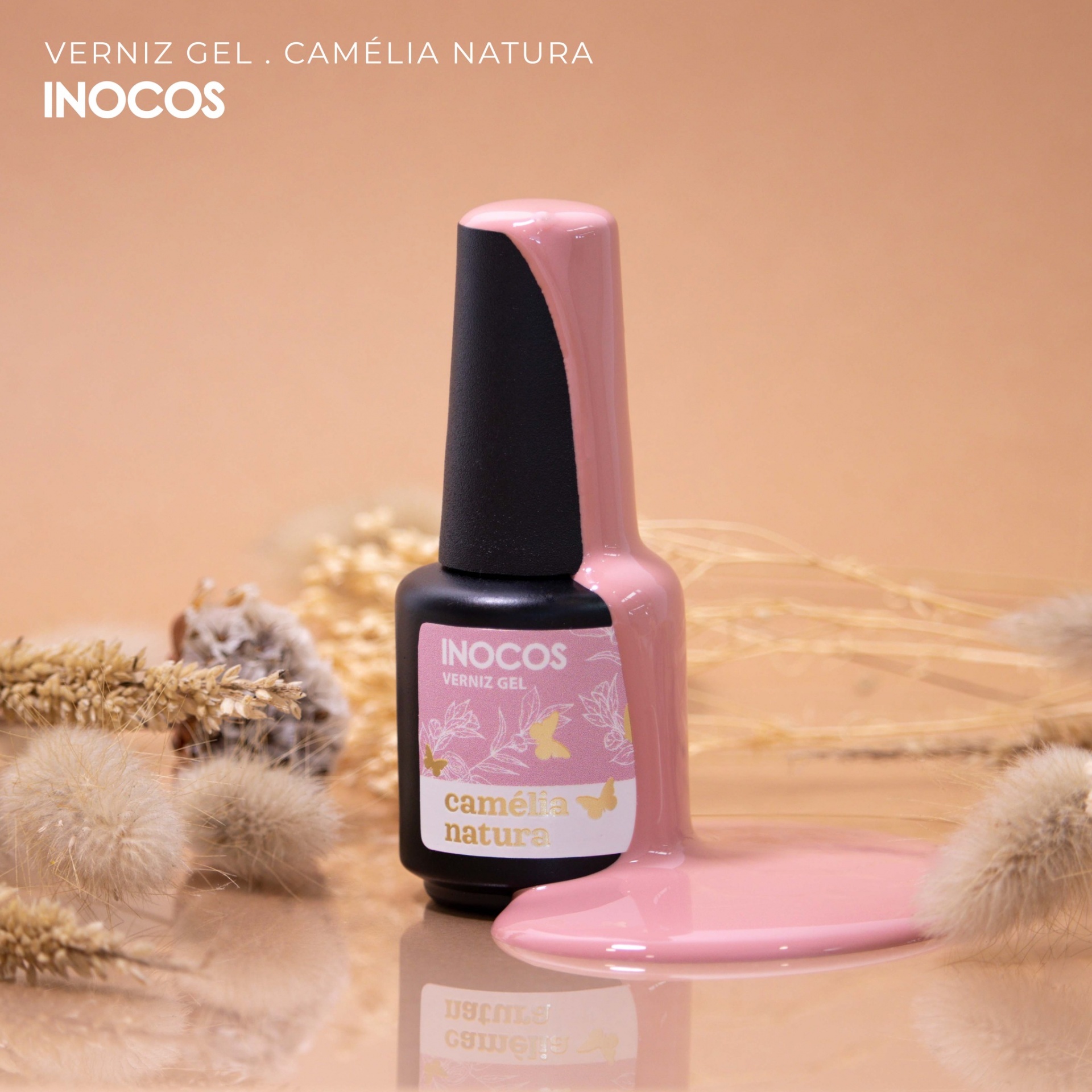 Verniz Gel Inocos – 293 - Camélia Natura 15ml Frasco preto de verniz gel rosa derramado com plantas secas ao fundo