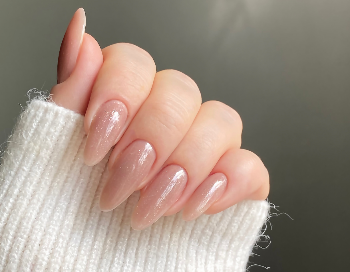 Mão com unhas rosa claro brilhante em manga branca de malha