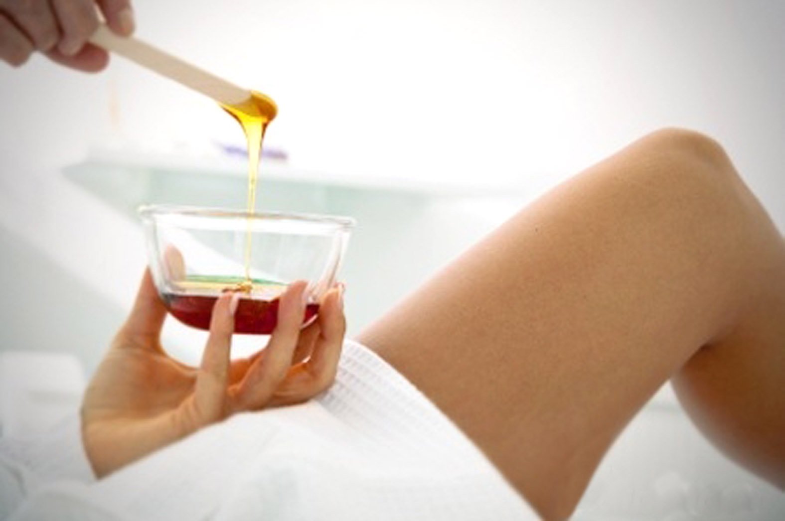 Mão segurando recipiente de vidro com mel dourado e perna visível em fundo claro