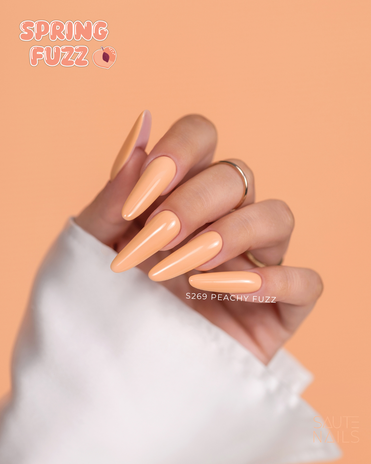 Verniz Gel Saute Nails S269 - Peachy Fuzz (Laranja Pêssego) Mão com unhas artificiais cor pêssego brilhante e texto SPRING FUZZ