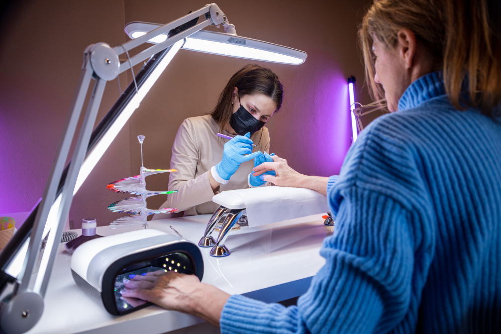 Cliente a fazer manicure com profissional em ambiente iluminado por luzes LED