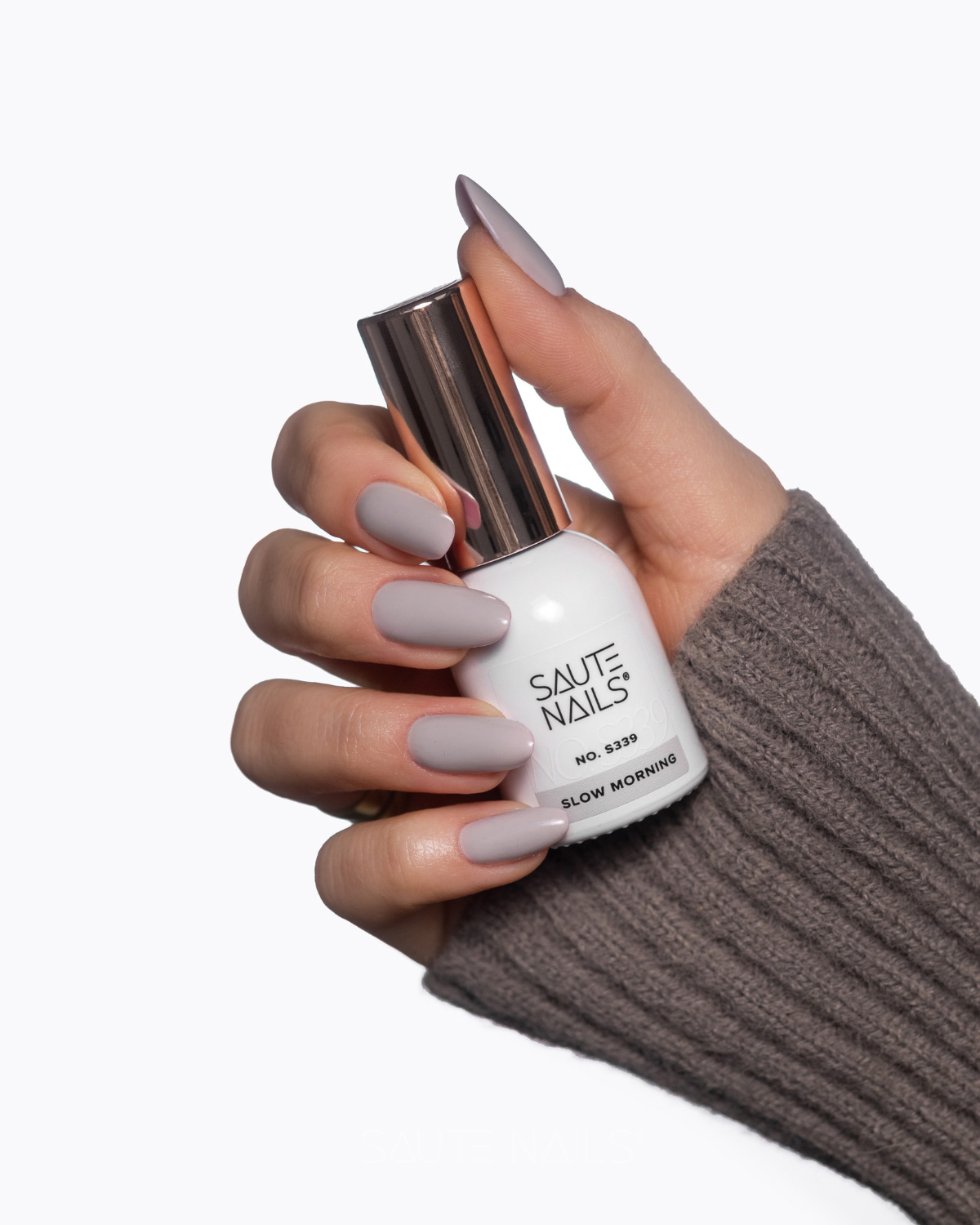 Verniz Gel Saute Nails S339 - Slow Morning (Cinzento Pastel Neutro) Mão com unhas pintadas segurando frasco de verniz SAUTE NAILS Slow Morning