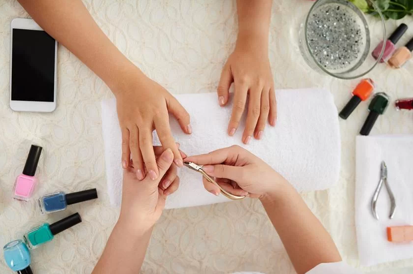 Manicure a cuidar de unhas com vernizes coloridos e ferramentas sobre toalha branca
