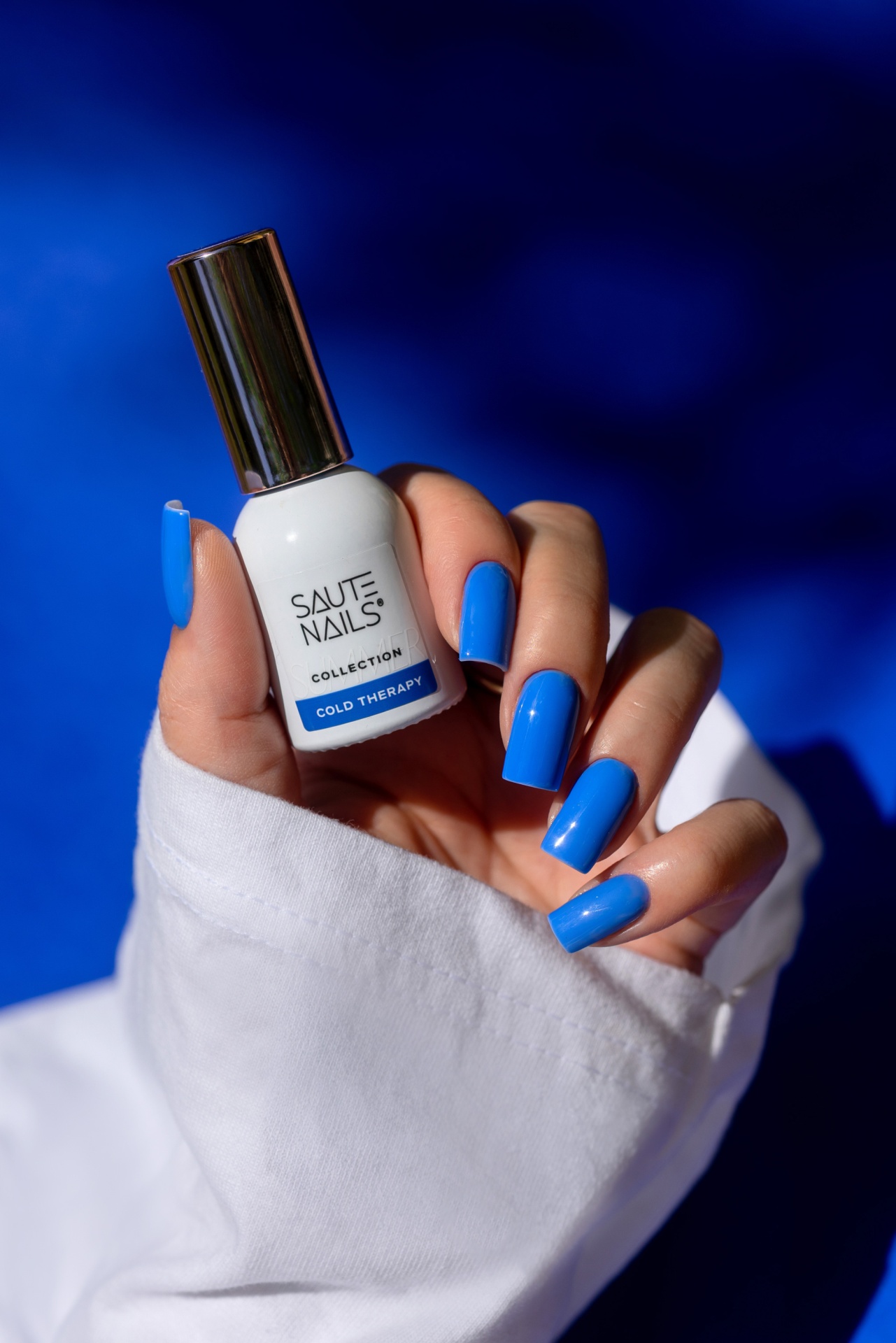 Verniz Gel Cold Therapy (Azul Royal Intenso) Verniz de unhas branco com tampa prateada e unhas azuis