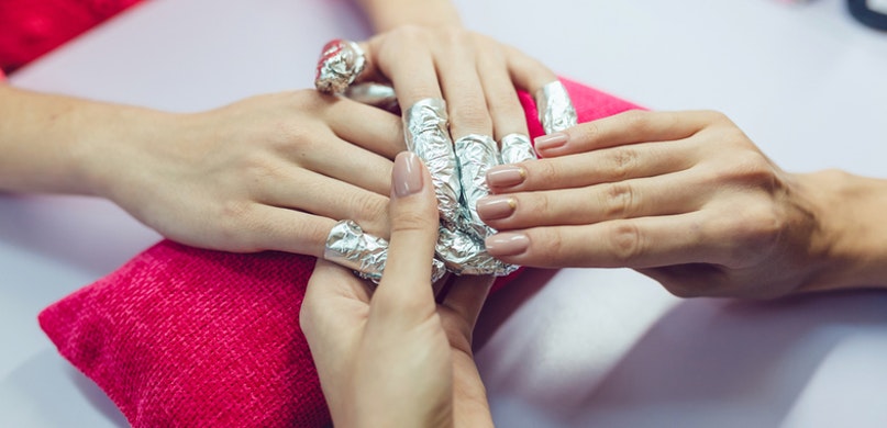 Mãos femininas com dedos enrolados em papel alumínio para tratamento de unhas.