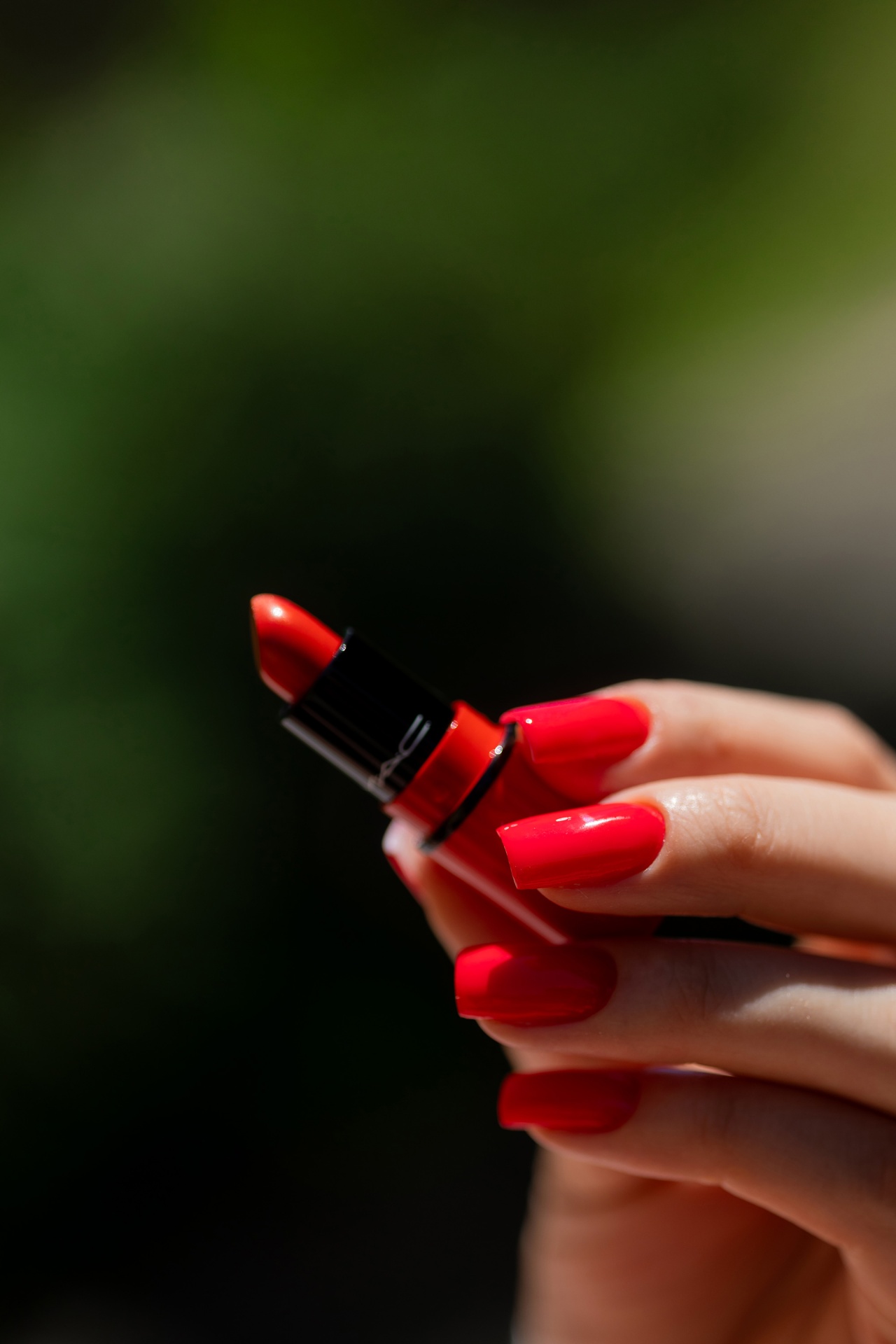 Verniz Gel Red Light Baby (Vermelho Laranja Néon) Batom vermelho vibrante em tubo preto com mão feminina unhas vermelhas