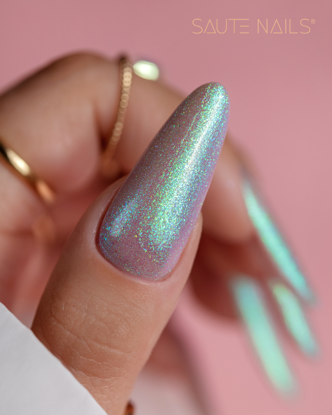 Verniz Gel Saute Nails S279 - Ursula (Azul Esverdeado com Partículas) Unha comprida com esmalte azul lilás iridescente e texto SAUTE NAILS numa mão com anéis.