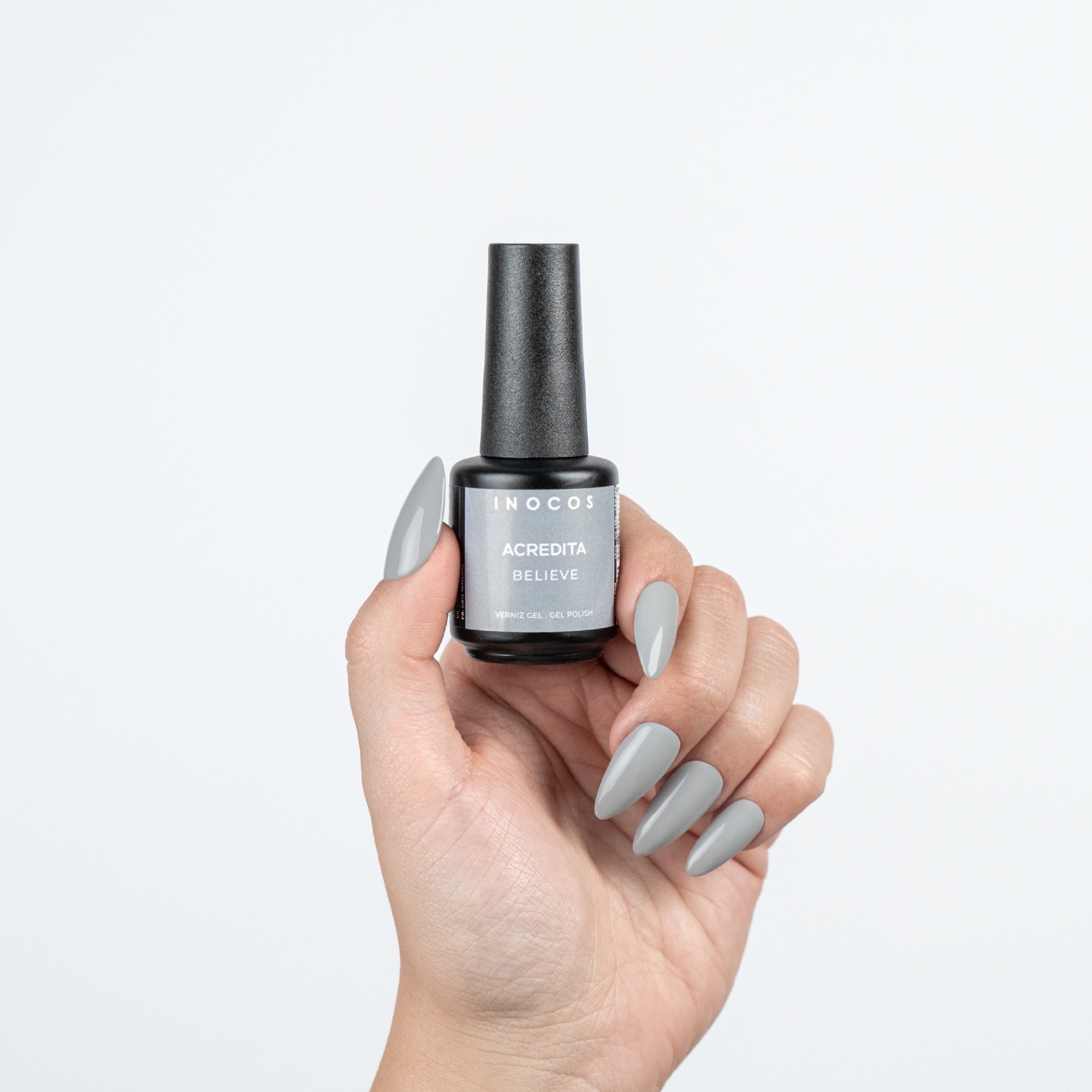 Verniz Gel Inocos 504 - Acredita Frasco de verniz gel INOCOS cinzento claro com unhas pintadas da mesma cor numa mão.