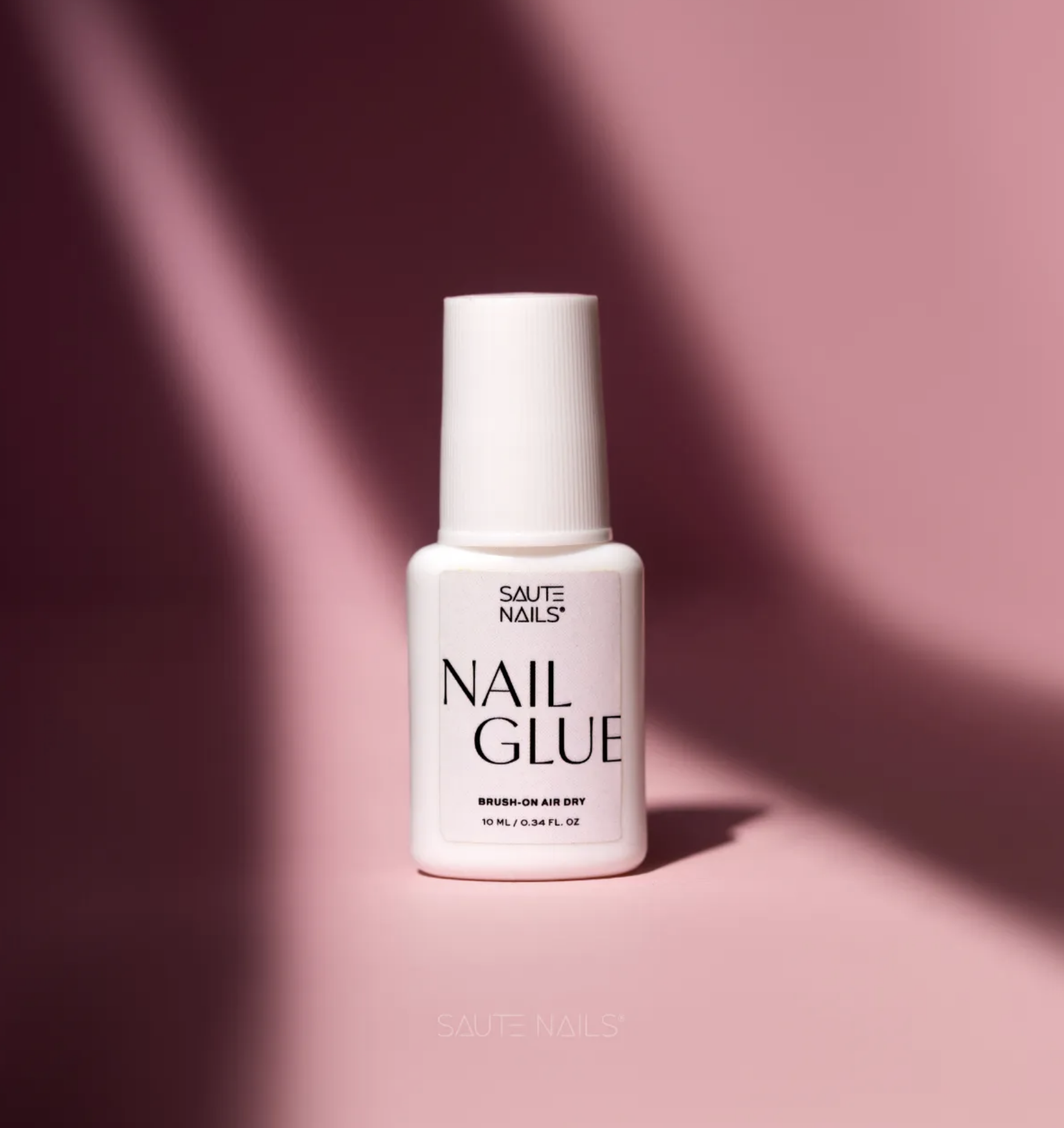 Cola para Tunnel Tips Saute Nails Frasco branco de cola para unhas com rótulo preto sobre fundo rosa
