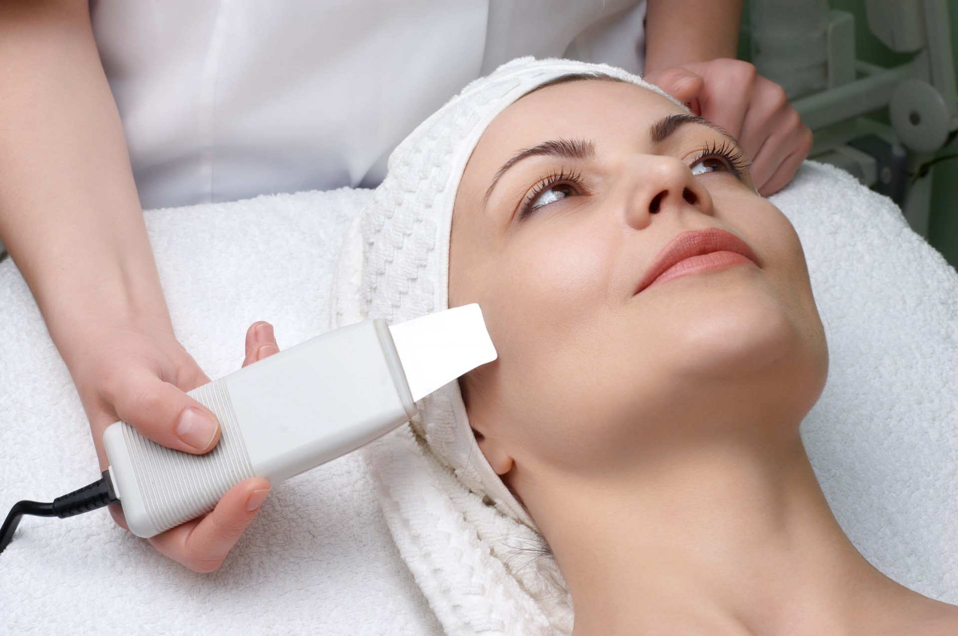 Mulher recebendo tratamento facial com aparelho branco em clínica