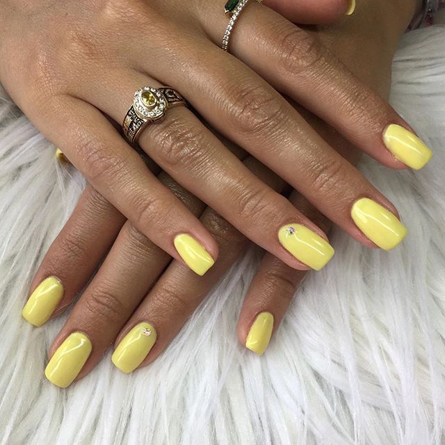 Verniz Gel Andreia 202 Mãos com unhas amarelas e anel de prata sobre tecido branco felpudo