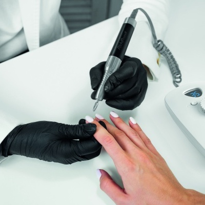 Aparelho elétrico para manicure usado por pessoa com luvas pretas num fundo branco