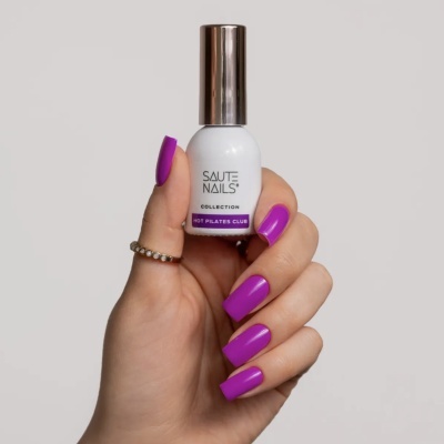 Mão segurando frasco de verniz de unhas branco com tampa prateada e texto SAUTE NAILS HOT PILATES CLUB