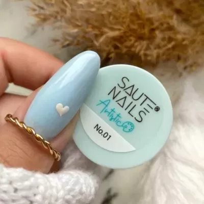 Frasco de verniz para unhas azul claro SAUTE NAILS Artistic No.01 segurado por mão com unha pintada azul claro e coração branco