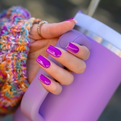 Mão com unhas roxas segurando copo térmico roxo