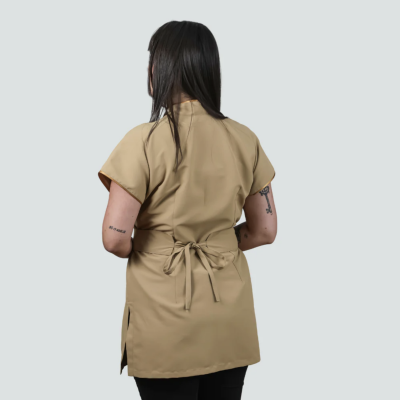 Pessoa de costas com bata bege e cinto amarrado, calças pretas, fundo cinza claro