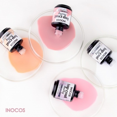 Frascos de verniz para unhas INOCOS com cores nude, rosa claro, branco e rosa médio sobre pratos transparentes