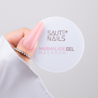Embalagem branca de gel para unhas SAUTE NAILS Marmalade Gel Macaroni, segurada por mão com unha rosa longa e anel brilhante.