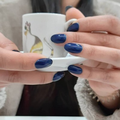 Caneca branca com imagem de gato segurada por mãos com unhas azuis