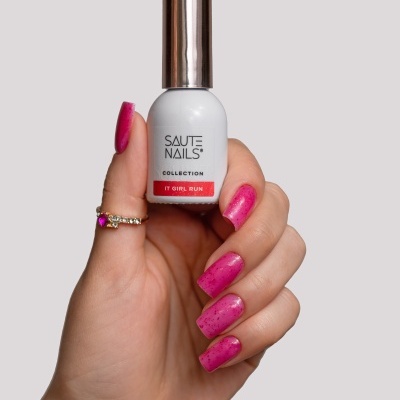 Frasco branco de verniz de unhas com tampa prateada segurado por mão com unhas cor rosa brilhantes