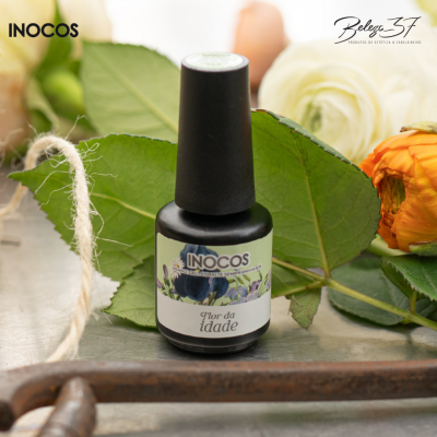 Frasco de verniz gel INOCOS Flor da Idade com folhas e flores ao fundo