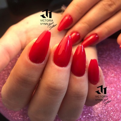 Mão feminina com unhas longas vermelhas brilhantes sobre fundo rosa brilhante