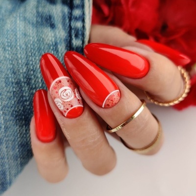 Unhas pintadas de vermelho com decoração floral e bolinhas, anéis dourados, fundo jeans e flores vermelhas