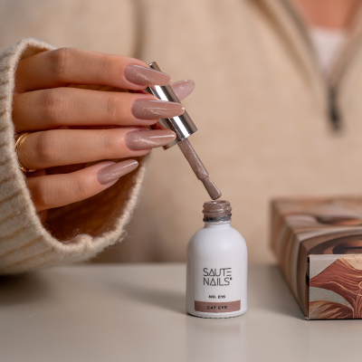 Verniz para unhas SAUTE NAILS cor CAT EYE com aplicador sendo segurado por uma mão com unhas compridas bege