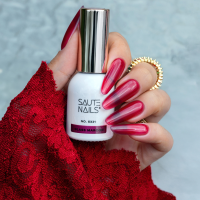 Frasco de verniz para unhas branco segurado por mão com unhas vermelhas longas e luva vermelha rendada.