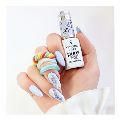 Mão com unhas azuis claras segurando verniz Victoria Vynn Pure Creamy Hybrid e usando anéis coloridos