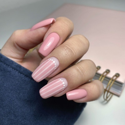 Unhas artificiais rosa claro com riscas brancas e pontos brancos em duas unhas