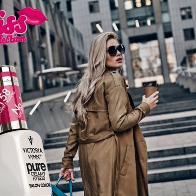 Frasco de verniz Victoria Vynn ao lado de mulher com casaco castanho e óculos escuros numa escadaria urbana.